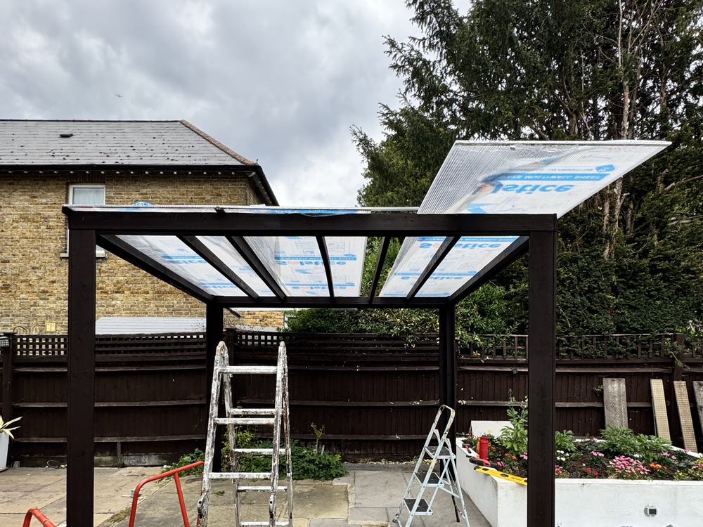 Pergola frame with roof sheets going on, ladders underneath