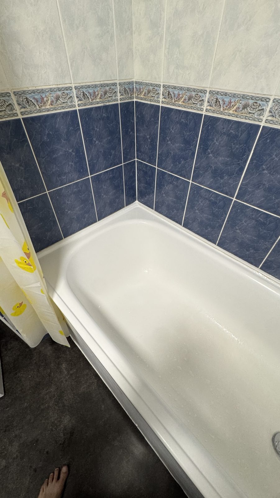 White bath against blue tiles with a clean new white silicone bead along the wall joint
