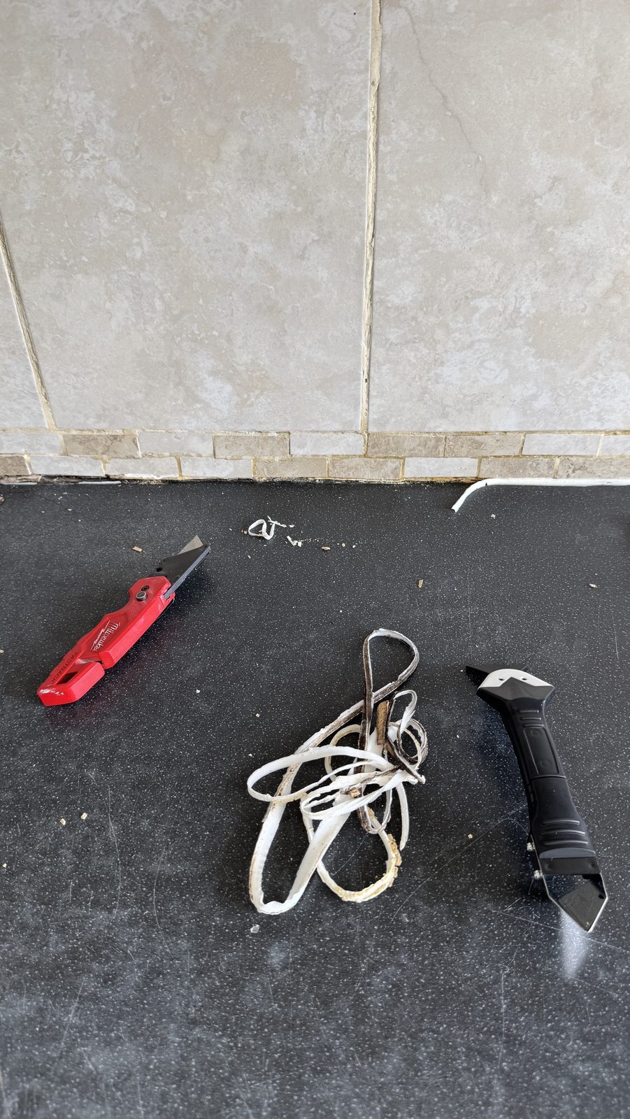 Strips of old discoloured silicone cut out from a kitchen worktop joint, next to a utility knife and a sealant removal tool