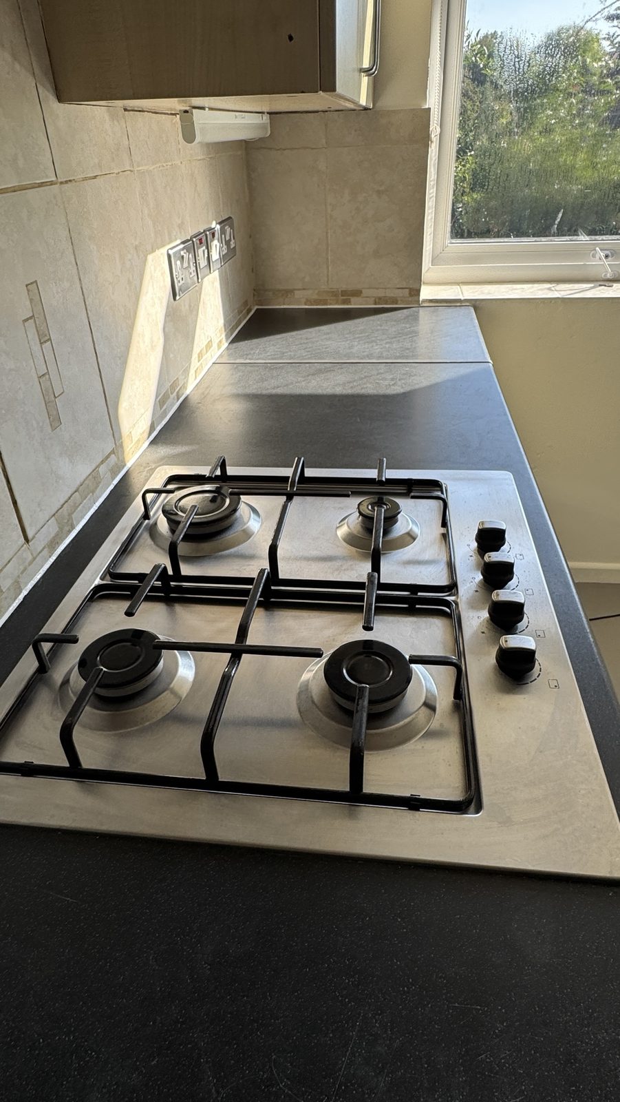Dark kitchen worktop with a gas hob and a neat new white silicone line along the tiled upstand