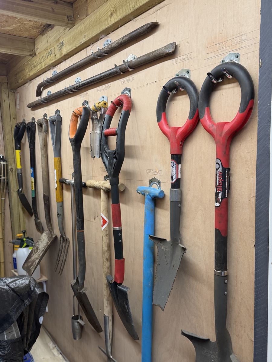 Shed after: spades, forks and bars each on its own labelled hook