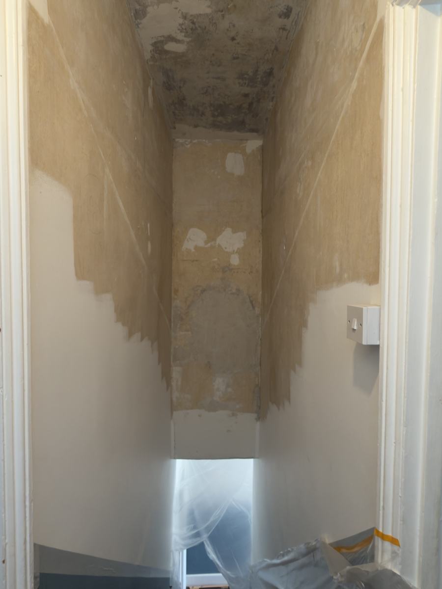 Stairwell before: walls stripped to bare plaster, damaged ceiling