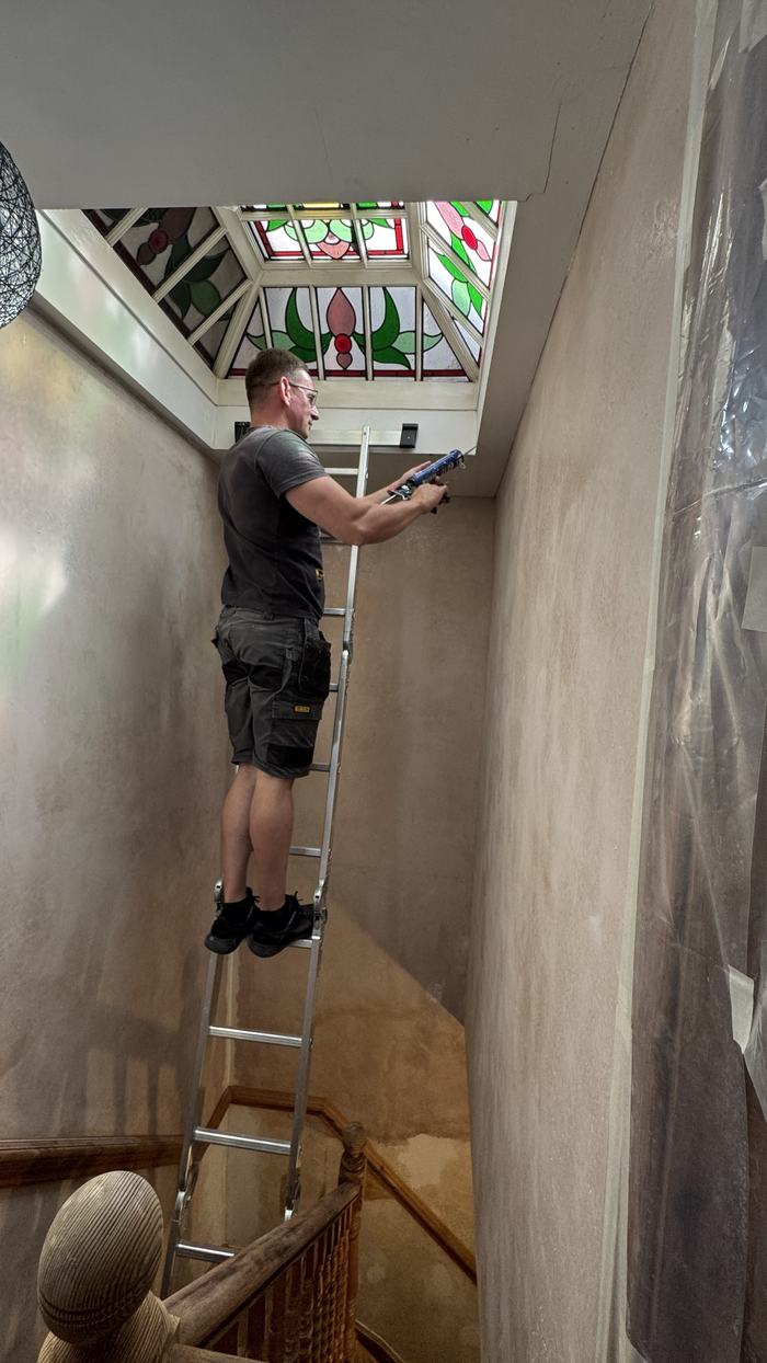 Alex on a ladder sealing around a skylight frame
