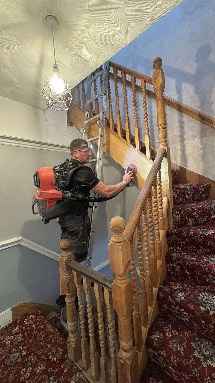 Alex sanding a staircase string with a backpack dust extractor